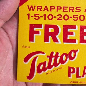 K&ouml;nnte beinhalten: Eine gelb-rote Vintage-Werbung f&uuml;r "Tattoo" Kaugummi. Der Text enth&auml;lt "WRAPPERS" und "FREE" in fetten roten Buchstaben. Das Copyright-Datum "&copy;1933" ist sichtbar. Die W&ouml;rter "Tattoo" und "PLA" sind ebenfalls sichtbar.