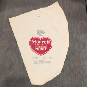 May include: A vintage white paper bag with a red heart-shaped logo that reads "Morrell Pride Pork Shoulder Picnic." The bag also includes text indicating the net weight in pounds and ounces, and the manufacturer, John Morrell & Co.