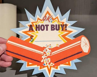 Könnte beinhalten: Ein sternförmiges Papierschild mit dem Text OK A HOT BUY! in dunkelvioletten Buchstaben. Das Design umfasst ein hellblaues und orangefarbenes Strahlenmuster sowie eine horizontale orangefarbene Balkengrafik mit einem zentralen Explosionseffekt.