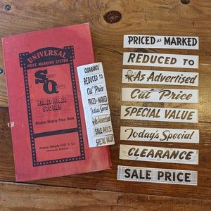 May include: A red book titled "Universal Price Marking System" with a white label that says "Clearance, Reduced to, Cut Price, Priced Marked, Today's Special, As Advertised, Sale Price, Special Value".  There are nine white labels with black text that say "Priced as Marked", "Reduced to", "As Advertised", "Cut Price", "Special Value", "Today's Special", "Clearance", "Sale Price".
