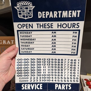 May include: A blue and white sign with the text "DEPARTMENT" and "OPEN THESE HOURS". The sign lists the hours of operation for each day of the week. The sign also includes the text "SERVICE SALES" and "PARTS USED CAR".
