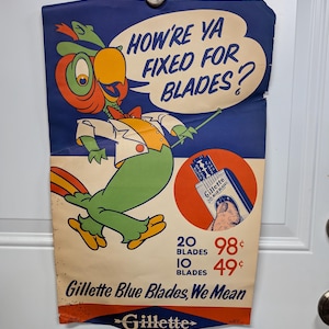 May include: A vintage advertisement for Gillette Blue Blades featuring a cartoon parrot with a speech bubble that says "How're ya fixed for blades?" The ad shows a price list for 20 blades for 98 cents and 10 blades for 49 cents. The ad also features a close-up of a Gillette Blue Blade razor.