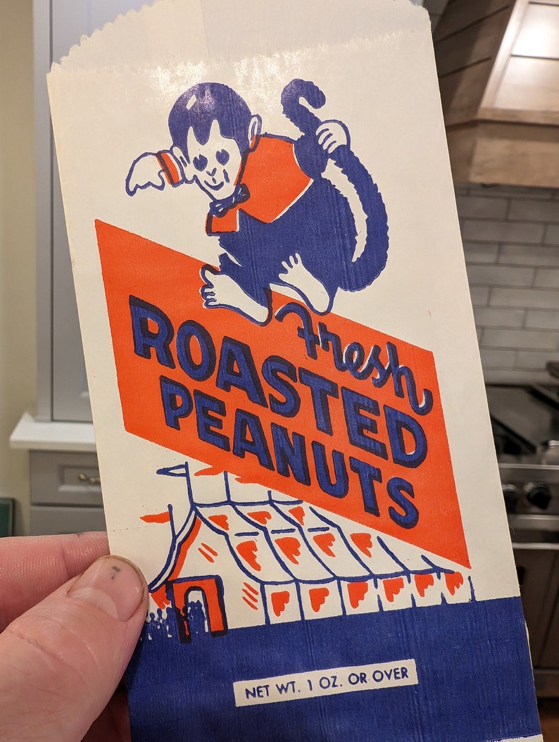 Peut inclure: Un sac en papier vintage avec un design bleu et rouge. Il repr&eacute;sente un singe de dessin anim&eacute; tenant une tente rouge et blanche ray&eacute;e avec le texte "Fresh Roasted Peanuts" et "Net Wt. 1 oz. or over".