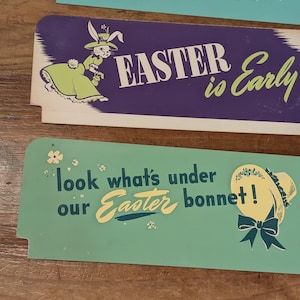 Könnte beinhalten: Drei Vintage-Osterschilder. Die Schilder sind rechteckig mit gewellten Kanten und weisen Pastellfarben auf. Ein Schild hat eine Hasenillustration und den Text "Easter is Everything Beautiful". Ein anderes sagt "Easter is Early". Das dritte sagt "look what's under our Easter bonnet!"