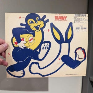Könnte beinhalten: Vintage Papierschnitt mit dem Bunny Enriched Bread Maskottchen. Der Cartoon-Hase ist blau und gelb und hält ein Brot. Der Markenname und die Anweisungen sind auf dem Papier aufgedruckt.