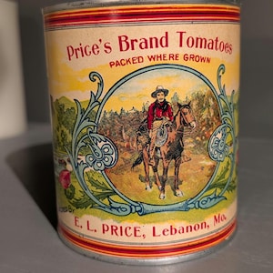 May include: Vintage Price's Brand Tomatoes can. The label features a cowboy on horseback within a blue and green decorative frame. The text reads "Price's Brand Tomatoes PACKED WHERE GROWN" and "E. L. PRICE, Lebanon, Mo."