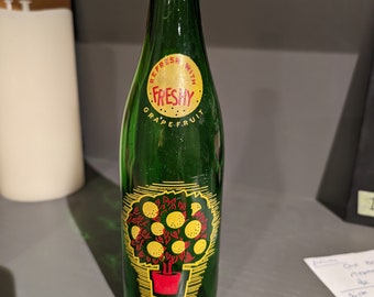 May include: A green glass bottle with a label that says "Refresh with Freshy Grapefruit". The bottle has a drawing of a potted grapefruit tree with yellow fruit.