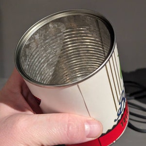May include: Empty metal can with a white label and red trim. The label has black and green text that reads "Telluride Brewing Company" and a graphic of a mountain range.