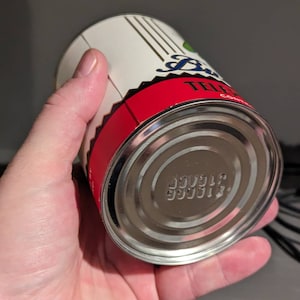 May include: A silver can with a red and white label. The label has the text "TELEPHONE" on it. The bottom of the can has a series of numbers printed on it.