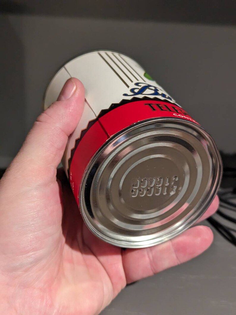 May include: A silver can with a red and white label. The label has the text "TELEPHONE" on it. The bottom of the can has a series of numbers printed on it.