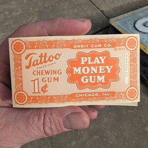 K&ouml;nnte beinhalten: Eine Vintage-Karte "Play Money Gum" von Orbit Gum Co. in Orange und Creme. Die Karte tr&auml;gt die Aufschrift "Tattoo Chewing Gum" und "1&cent;" mit dem Text "Chicago, Ill." und dem Jahr "1933".