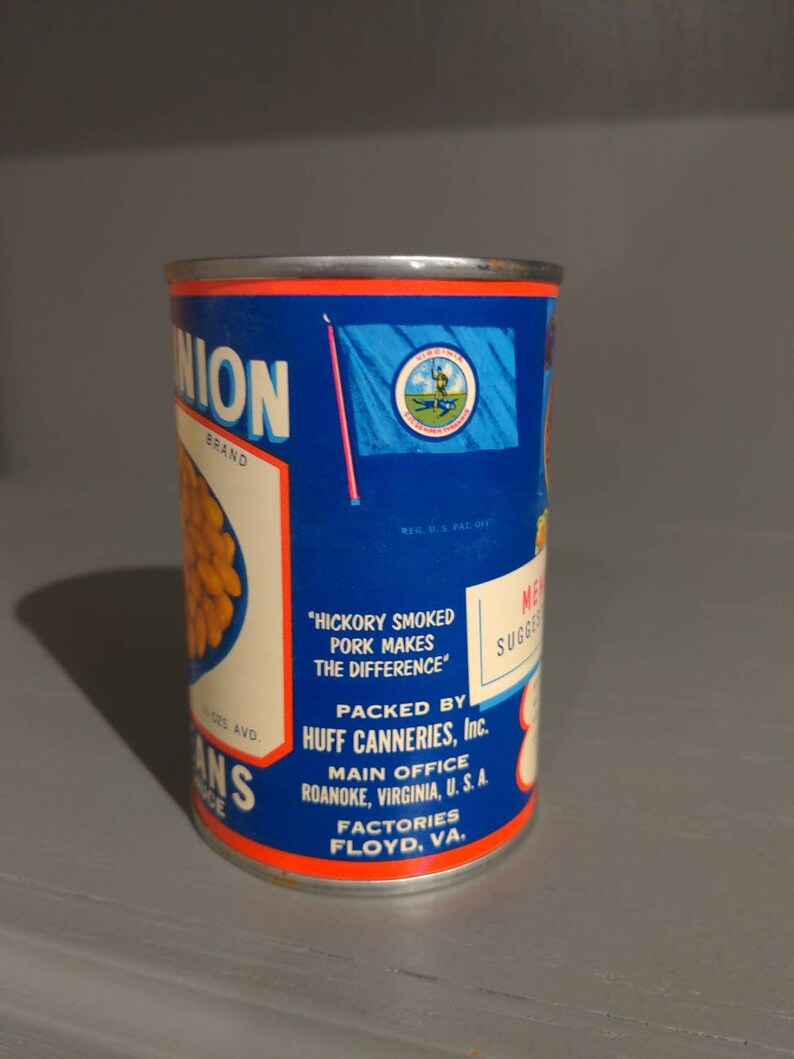 May include: A blue and red can of Union brand canned beans. The can has a label with the text "Hickory Smoked Pork Makes The Difference" and "Packed by Huff Canneries, Inc.". The label also includes the company's main office location in Roanoke, Virginia, U.S.A. and factory location in Floyd, Virginia.
