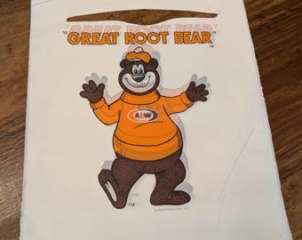 May include: White paper bag with a brown bear wearing an orange sweater with the A&W logo. The bear is holding its arms out and has a red and white hat. The text "Great Root Bear" is printed on the bag.