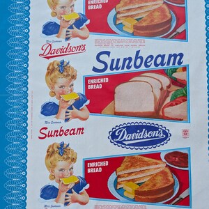 Op de afbeelding: Vintage Sunbeam broodadvertentie met een jong meisje dat een sneetje brood eet. De advertentie bevat de tekst "Sunbeam", "Davidson's" en "Enriched Bread". Het ontwerp heeft een rood, wit en blauw kleurenschema, met afbeeldingen van toast en boter.