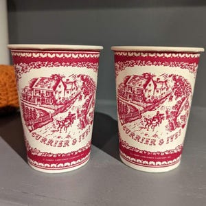 May include: Two red and white paper cups with a vintage design featuring a small town scene and the text "Currier & Ives".