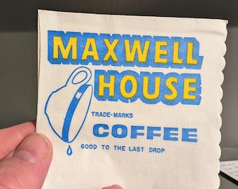 May include: A white paper coffee napkin with a scalloped edge. The napkin features the words "MAXWELL HOUSE" in yellow block letters with a blue outline. Below is a blue coffee cup graphic and the word "COFFEE". The text "GOOD TO THE LAST DROP" is also printed.