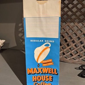 May include: A vintage paper bag for Maxwell House Coffee, featuring a blue background with a white coffee cup and orange trim. The bag reads "Good to the Last Drop" and "Regular Grind". The text also includes "High Grade - One Pound Net Weight - 454 Grams" and "General Foods Corporation - Address New York 17, N.Y."