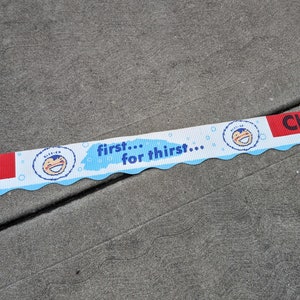 Puede incluir: Una pancarta azul y blanca con una franja roja y un personaje de dibujos animados con un sombrero azul y blanco. La pancarta dice "first... for thirst..."