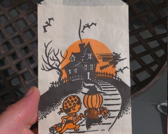 Könnte beinhalten: Vintage Halloween-Trick-or-Treat-Beutel mit einer schwarz-orangenen Illustration eines Hauses, einer fliegenden Hexe und zwei Kindern, die einen Weg hinaufgehen. Der Beutel ist weiß mit dem Aufdruck "Trick or Treat" in Schwarz.