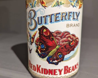 May include: A can of Butterfly Brand Red Kidney Beans. The label features a large red and yellow butterfly illustration with the brand name in blue and gold. The top of the can has a gold border with butterfly illustrations.