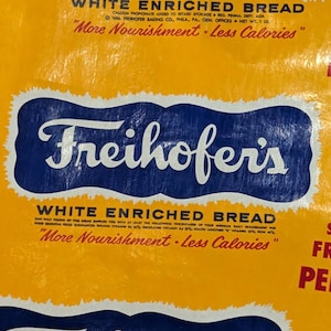May include: Close-up of a vintage Freihofer's White Enriched Bread bag. The bag has a yellow background with blue rectangular labels. The labels feature the brand name and text: "More Nourishment - Less Calories."