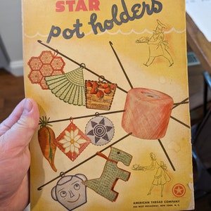 Könnte beinhalten: Ein Vintage-Buchcover mit dem Titel "STAR pot holders" und dem Text "BOOK No. 32" und "10 CENTS". Das Cover zeigt Illustrationen verschiedener gehäkelter Topflappen, darunter ein fächerförmiger, eine Gänseblümchen, ein Stern und ein Pferd. Das Cover zeigt auch Illustrationen von zwei Personen, eine hält einen Teller mit Essen und die andere hält einen Topf.