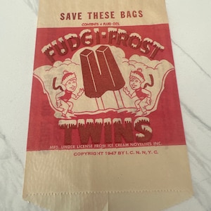 Könnte beinhalten: Ein roter und weißer Papierbeutel mit dem Aufdruck "Fudgi-Frost Twins". Der Beutel zeigt zwei Comicfiguren, die Eis am Stiel halten. Der Text "Save These Bags" und "Contents 4 Fluid Ozs." ist oben auf dem Beutel gedruckt. Der Text "Mfd. Under License From Ice Cream Novelties Inc." und "Copyright 1947 By I.C.N. N, Y.C." ist unten auf dem Beutel gedruckt.