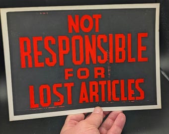 Op de afbeelding: Een rechthoekig bord met een zwarte achtergrond en een witte rand met de rode tekst NOT RESPONSIBLE FOR LOST ARTICLES in een vetgedrukt bloklettertype. Het bord is horizontaal georiënteerd en toont duidelijke, contrastrijke letters.