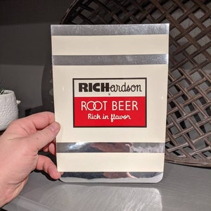 May include: A vintage-style silver and white striped cardboard box with a red and white label that reads "Richardson Root Beer Rich in Flavor".