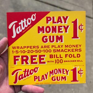 K&ouml;nnte beinhalten: Eine gelb-rote Vintage-Karte "Tattoo Play Money Gum". Die Karte enth&auml;lt Text wie "Play Money Gum", "Wrappers are Play Money" und "Free Bill Fold". Die Karte hat einen Preis von 1&cent; und das Logo der Orbit Gum Company.