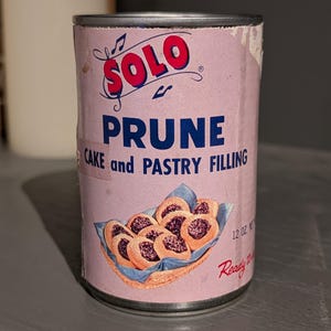 May include: A vintage can of Solo Prune Cake and Pastry Filling. The can is pink with red and blue text and a graphic of prune pastries. The can is 12 oz.