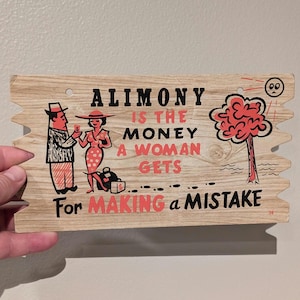May include: A wooden sign with a humorous saying about alimony. The sign features a cartoon couple, a tree, and the text "Alimony is the money a woman gets for making a mistake."