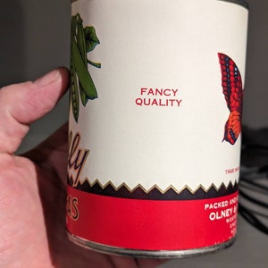 May include: A red and white can of peas with a green pea pod and a butterfly design. The can says "Fancy Quality" and "Packed and Distributed by Olney & Sons, Inc. West Chester, PA".