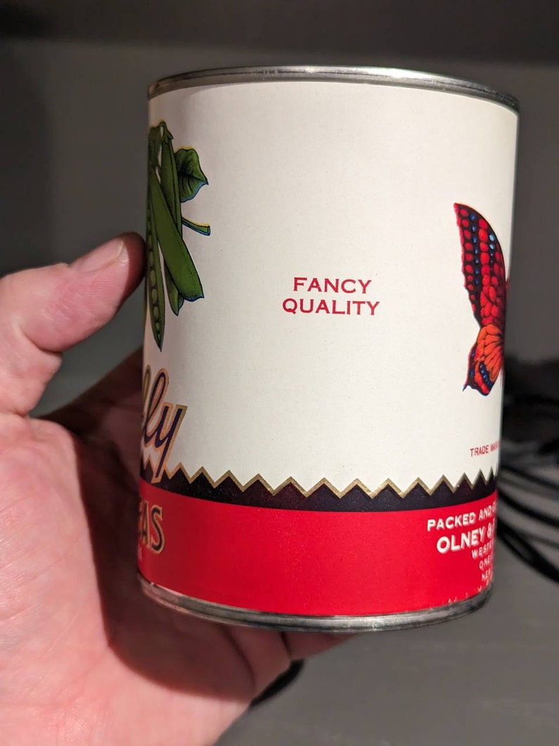 May include: A red and white can of peas with a green pea pod and a butterfly design. The can says "Fancy Quality" and "Packed and Distributed by Olney & Sons, Inc. West Chester, PA".