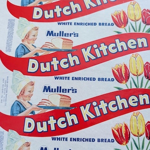 May include: Vintage Dutch Kitchen bread packaging featuring a smiling girl in a Dutch bonnet holding a tray of bread. The packaging has a red banner with the words "Dutch Kitchen" and "White Enriched Bread". Tulips decorate the background.