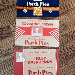May include: Three vintage Porth Pies labels featuring a cartoon chef. The top label is blue with white text and a price of 25 cents. The middle label is brown with red text and says "Cocoanut Cream". The bottom label is red with white text and says "Fresh Raspberry".
