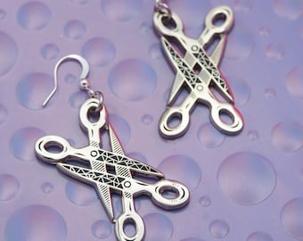 May include: A pair of silver earrings shaped like scissors with a black and white geometric pattern.