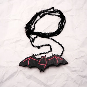 May include: A black bat pendant necklace with red eyes and wings. The necklace is on a black chain.