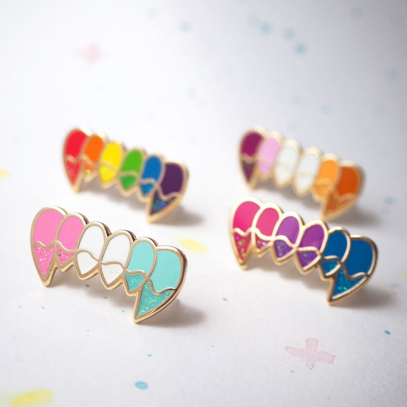 May include: Five enamel pins shaped like ice cream cones. Each cone is a different color: pink, white, light blue, red, orange, yellow, green, blue, purple, and dark blue. The pins have gold accents and glitter.