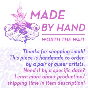 Puede incluir: Una ilustraci&oacute;n rosa y morada de dos manos sosteniendo una llama. El texto "MADE BY HAND WORTH THE WAIT" est&aacute; debajo de la imagen. El texto "Thanks for shopping small! This piece is handmade to order, by a pair of queer artists. Need it by a specific date? Learn more about production/shipping time in item description!" est&aacute; debajo de la imagen.