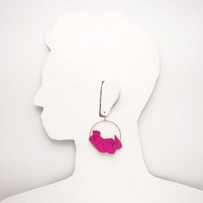 May include: A pair of pink hoop earrings with a gold hoop and a pink figure of two people holding hands.