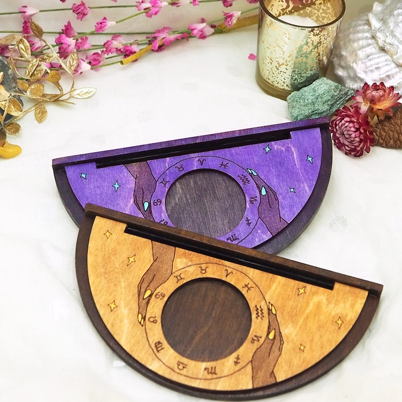 Puede incluir: Dos ruedas zodiacales de madera con madera te&ntilde;ida de morado y marr&oacute;n. La rueda superior tiene un fondo morado con estrellas y la rueda inferior tiene un fondo marr&oacute;n con estrellas. Ambas ruedas tienen s&iacute;mbolos del zod&iacute;aco y manos.