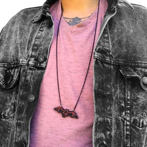 May include: A black chain necklace with a black bat pendant. The bat has red accents on the wings.