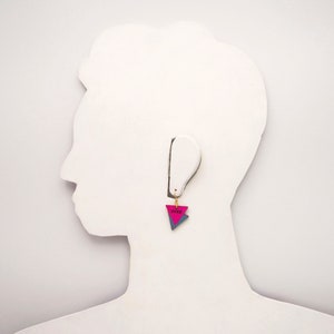 May include: Pink and blue triangle shaped earring with the word "DYKE" written on it.