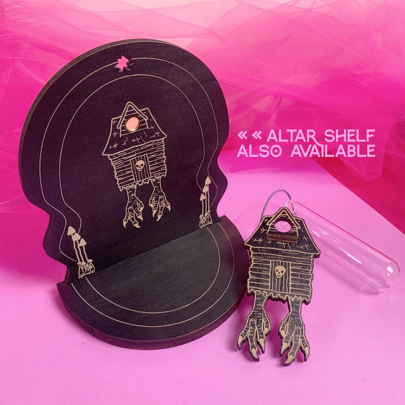 May include: A black wooden altar shelf and matching charm. The shelf is skull-shaped with a house design and the text "ALTAR SHELF ALSO AVAILABLE". The charm is a house with bird feet and a skull.