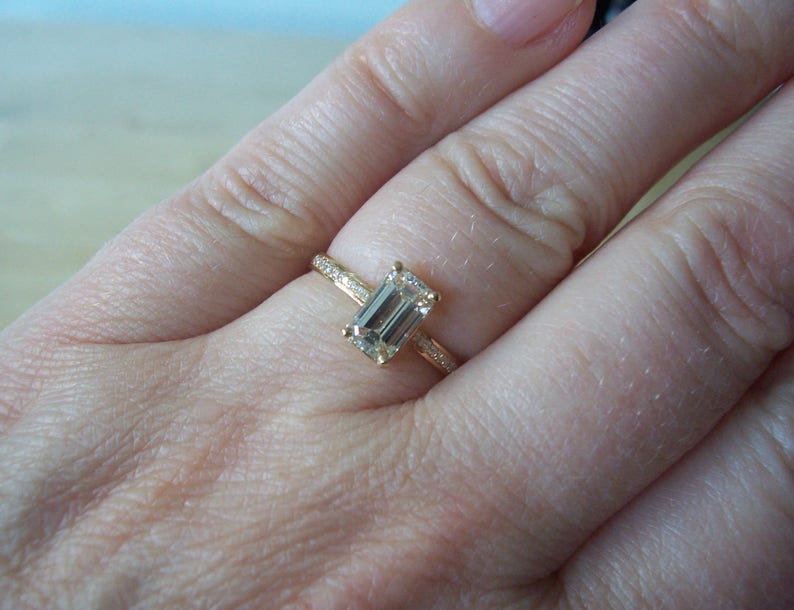 May include: A gold ring with an emerald cut gemstone. The ring is on a person's finger.
