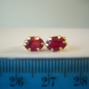 May include: A pair of gold earrings with oval-shaped red ruby stones.