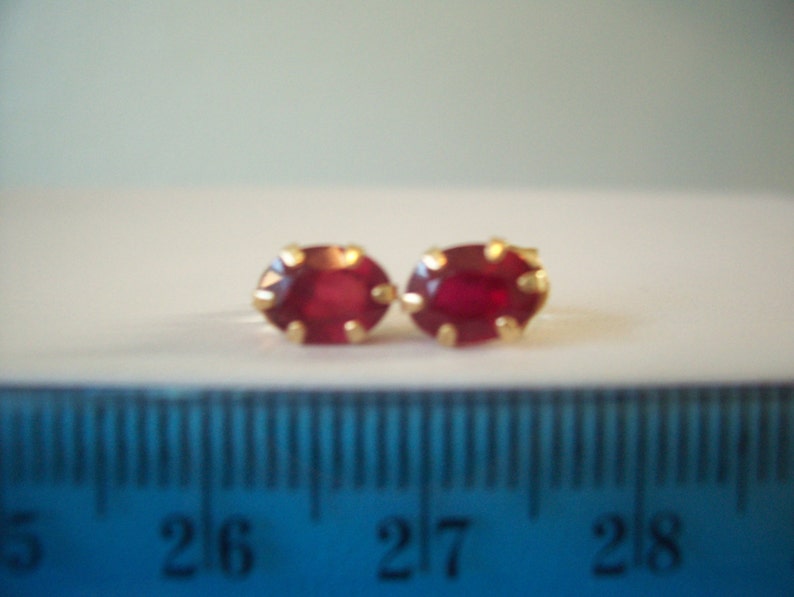 May include: A pair of gold earrings with oval-shaped red ruby stones.