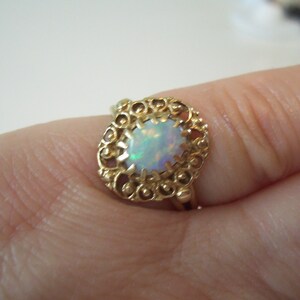 May include: A gold ring with an oval-shaped opal gemstone set in a filigree design.