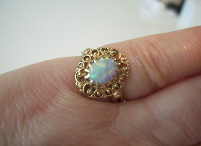 May include: A gold ring with an oval-shaped opal gemstone set in a filigree design.